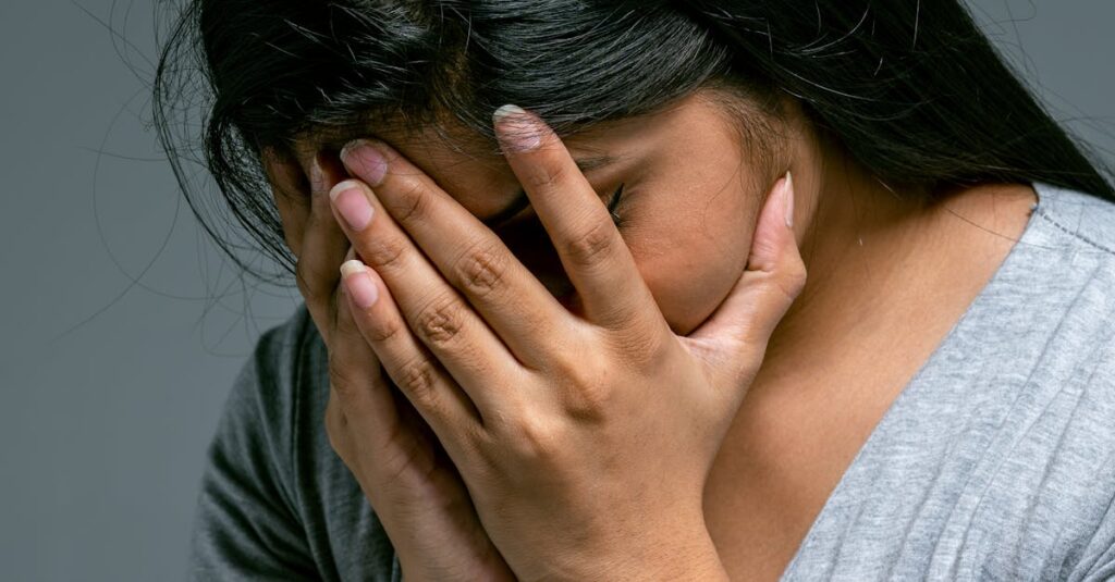 A woman hides her face in hands showing deep emotion and sadness in a studio setting.